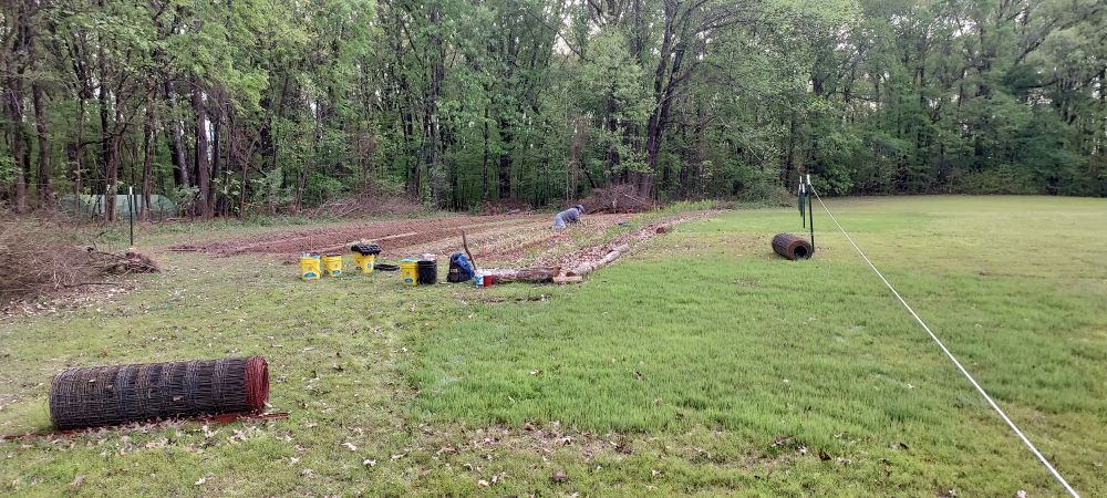 Nearly finished beds in the Playground.  Amanda works in the mid-distance.  The forest behind is filling in with spring leaves, and a greenhouse nestles just in view.  Fencing lays ready to be installed.